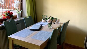 Un coin repas avec une table en bois, des chaises vertes, un vase de fleurs et un luminaire suspendu.