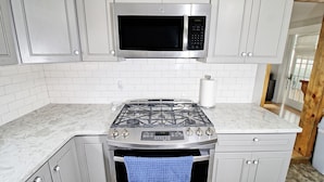 A kitchen with white cabinets, a stainless steel microwave, a gas stove, and a paper towel holder.