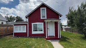 A red house with a white door and windows, a covered porch, and a well-maintained lawn.