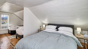 A bedroom with a large bed, two bedside tables with lamps, a window with blinds, and a view of the outside.