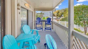 Een overdekt balkon met turquoise stoelen en een tafel, met uitzicht op een woonwijk met huizen en groen.