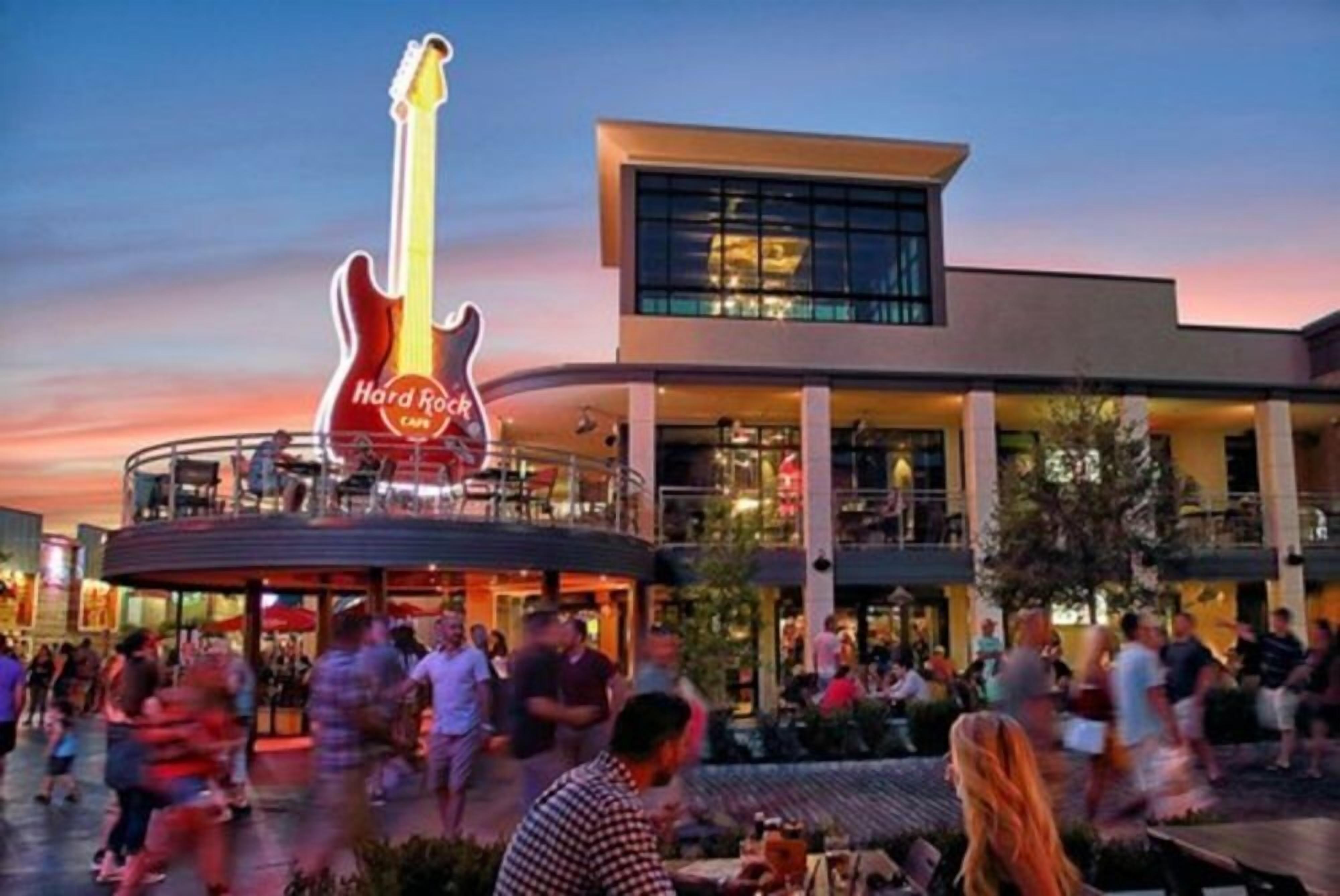 A Hard Rock Cafe with a large guitar sign, outdoor seating, and a modern building facade.