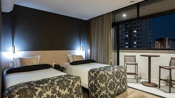 Habitación de hotel con dos camas, un balcón con sillas y vista a la ciudad de noche.