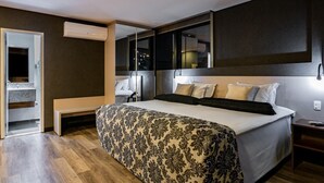 Habitación de hotel moderna con una cama grande, una banca empotrada, una mesita pequeña y un ventanal amplio.