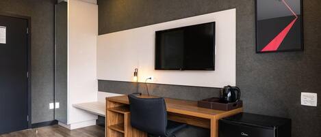 A modern office space with a wooden desk, black office chair, and a mounted flat-screen TV.