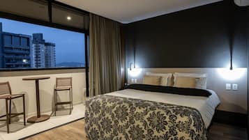 A hotel room with a large bed, a balcony with two chairs, and a city view.