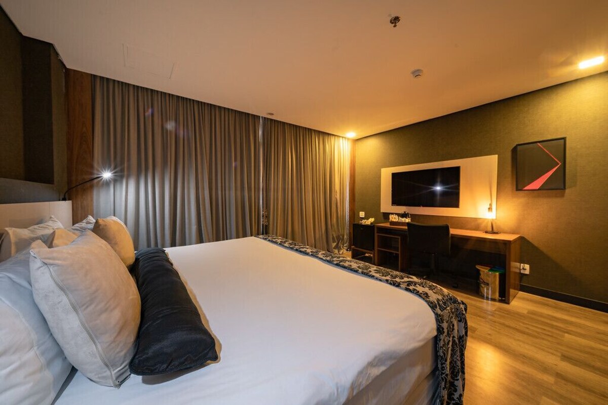 A hotel room with a large bed, a desk, a television, and a curtain.