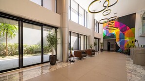 Un vestíbulo amplio con ventanas grandes, un mural de arte moderno y una recepción.