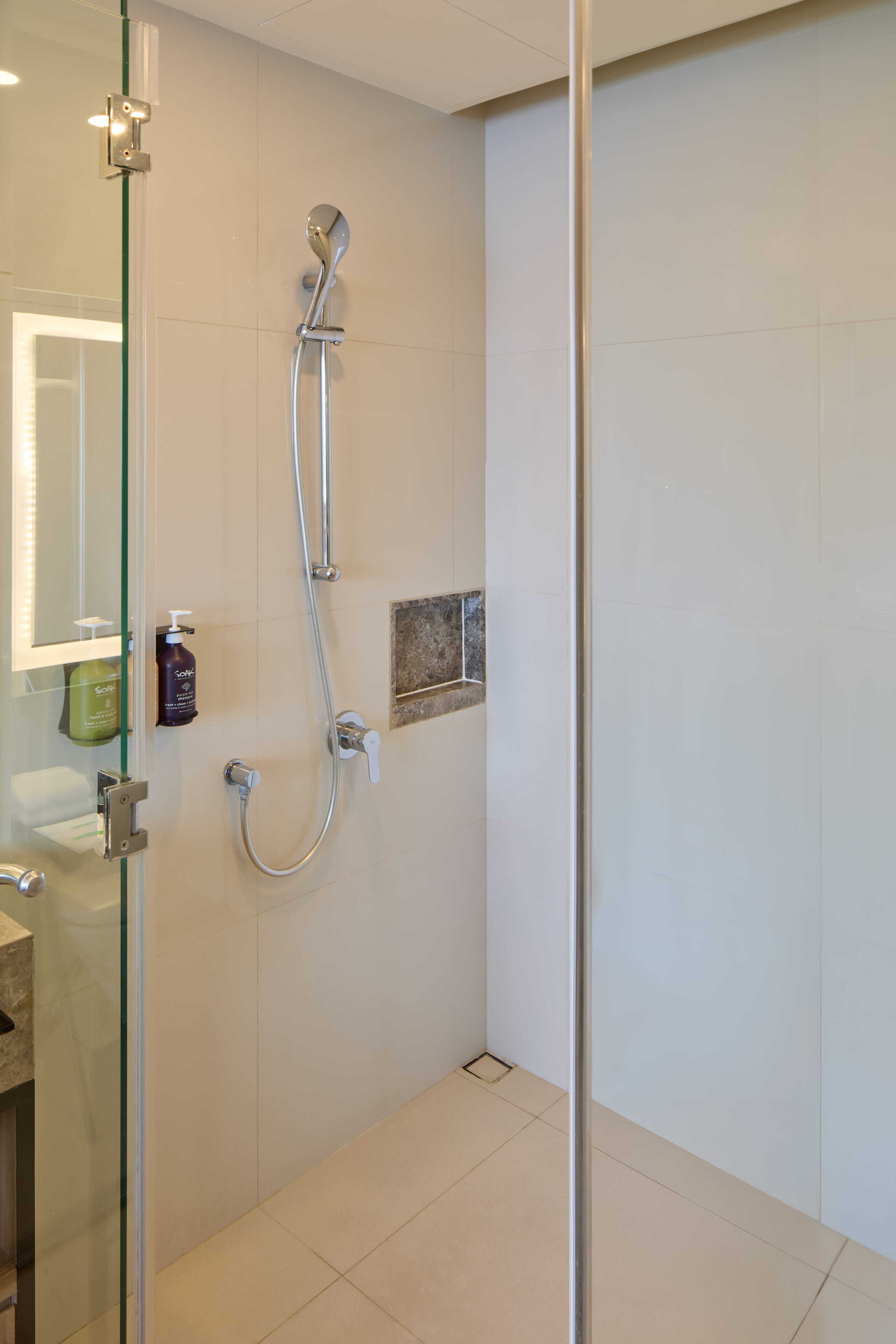 Et moderne badeværelse med en glas brusekabine, håndbruser og en lille hylde med toiletartikler.