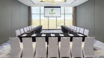 A conference room with a long table, white chairs, and a large screen displaying the Holiday Inn logo.