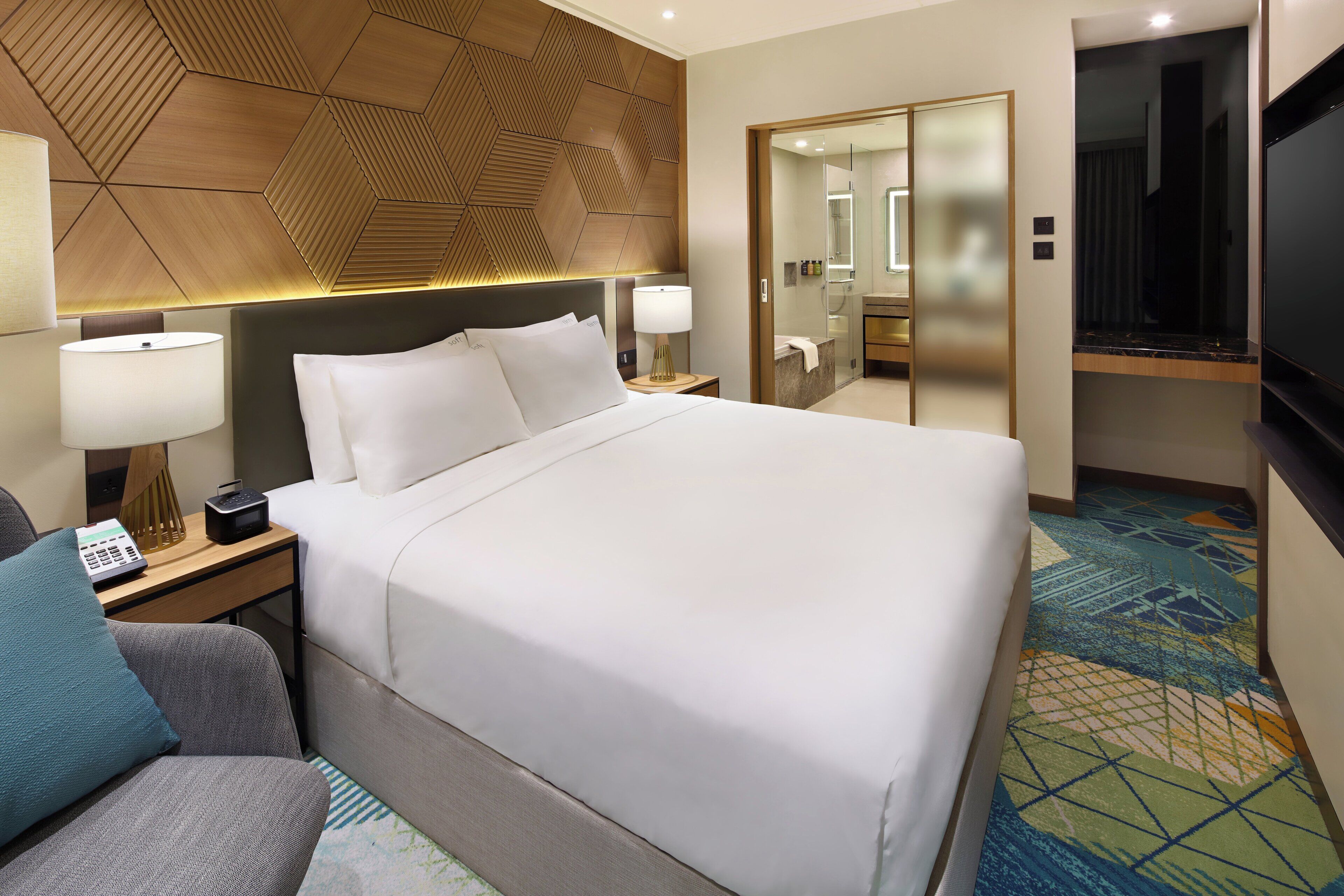 Une chambre d’hôtel dotée d’un grand lit, de tables de chevet, d’un bureau, d’une chaise, d’une télévision et d’une salle de bain avec une douche à parois de verre.