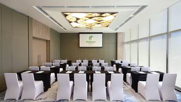 A conference room with multiple tables and chairs, a large screen displaying the hotel name, and a patterned carpet.