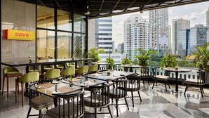 A modern restaurant with a city view, featuring a mix of round and rectangular tables, green and black chairs, and a prominent 'Sevii' sign on the wall. - Holiday Inn Cebu City by IHG (Cebu City)