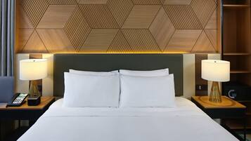 Une chambre d’hôtel avec un grand lit, deux tables de chevet avec des lampes, un téléphone et une tête de lit ornée d’un motif géométrique.