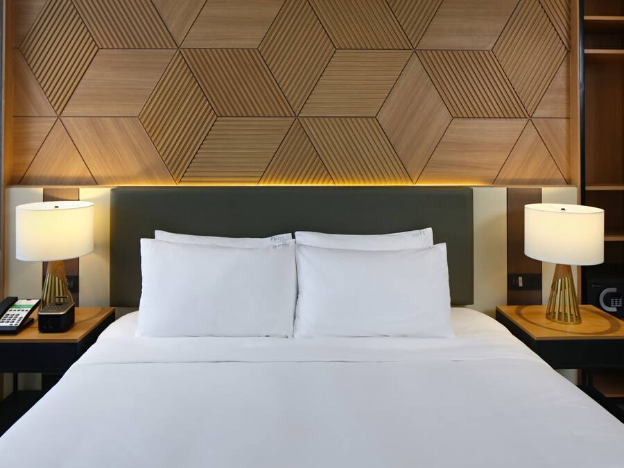 Une chambre d’hôtel avec un grand lit, deux tables de chevet avec des lampes, un téléphone et une tête de lit ornée d’un motif géométrique.