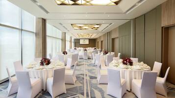 A banquet hall with round tables set for dining, white chairs, and floral centerpieces.