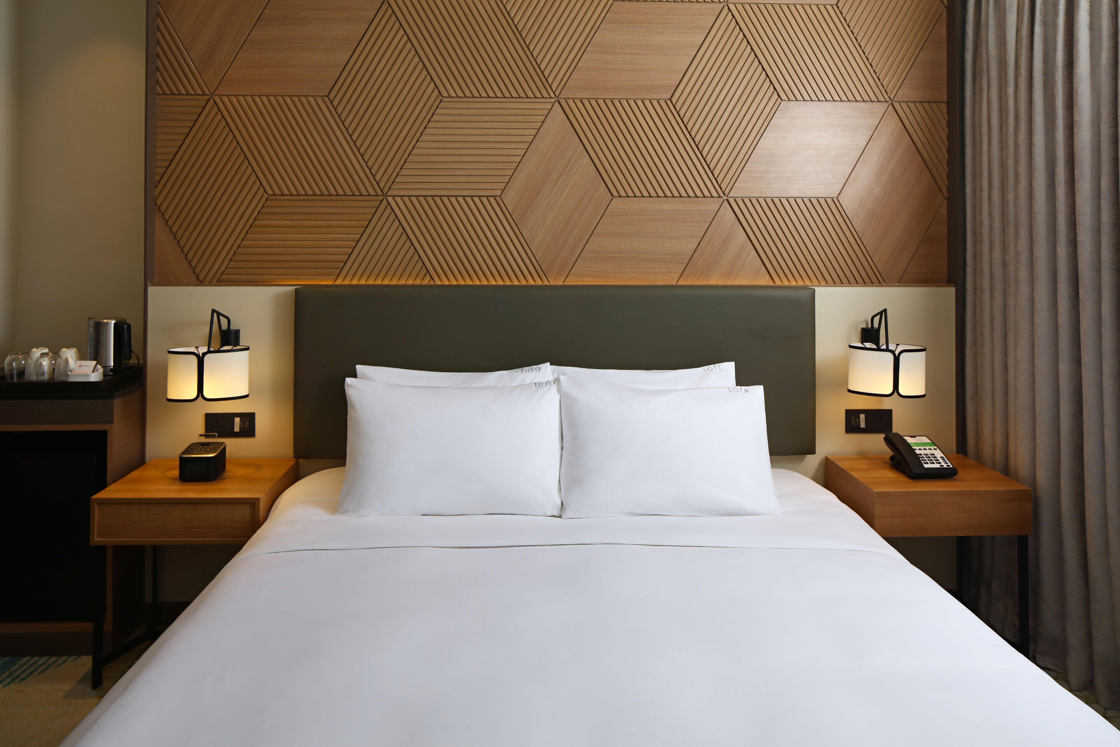 A hotel room with a large bed, two bedside tables with lamps, a wooden headboard, and a geometric wall pattern.