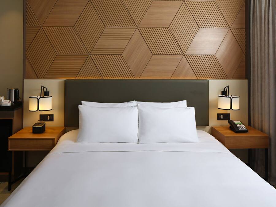 A hotel room with a large bed, two bedside tables with lamps, a wooden headboard, and a geometric wall pattern.