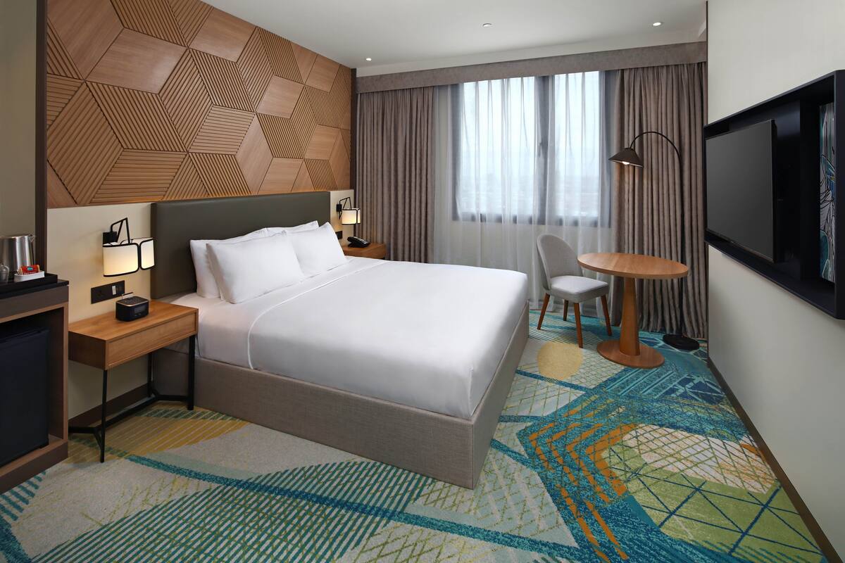 Une chambre d’hôtel avec un grand lit, un bureau avec une lampe, une télévision et une chaise.