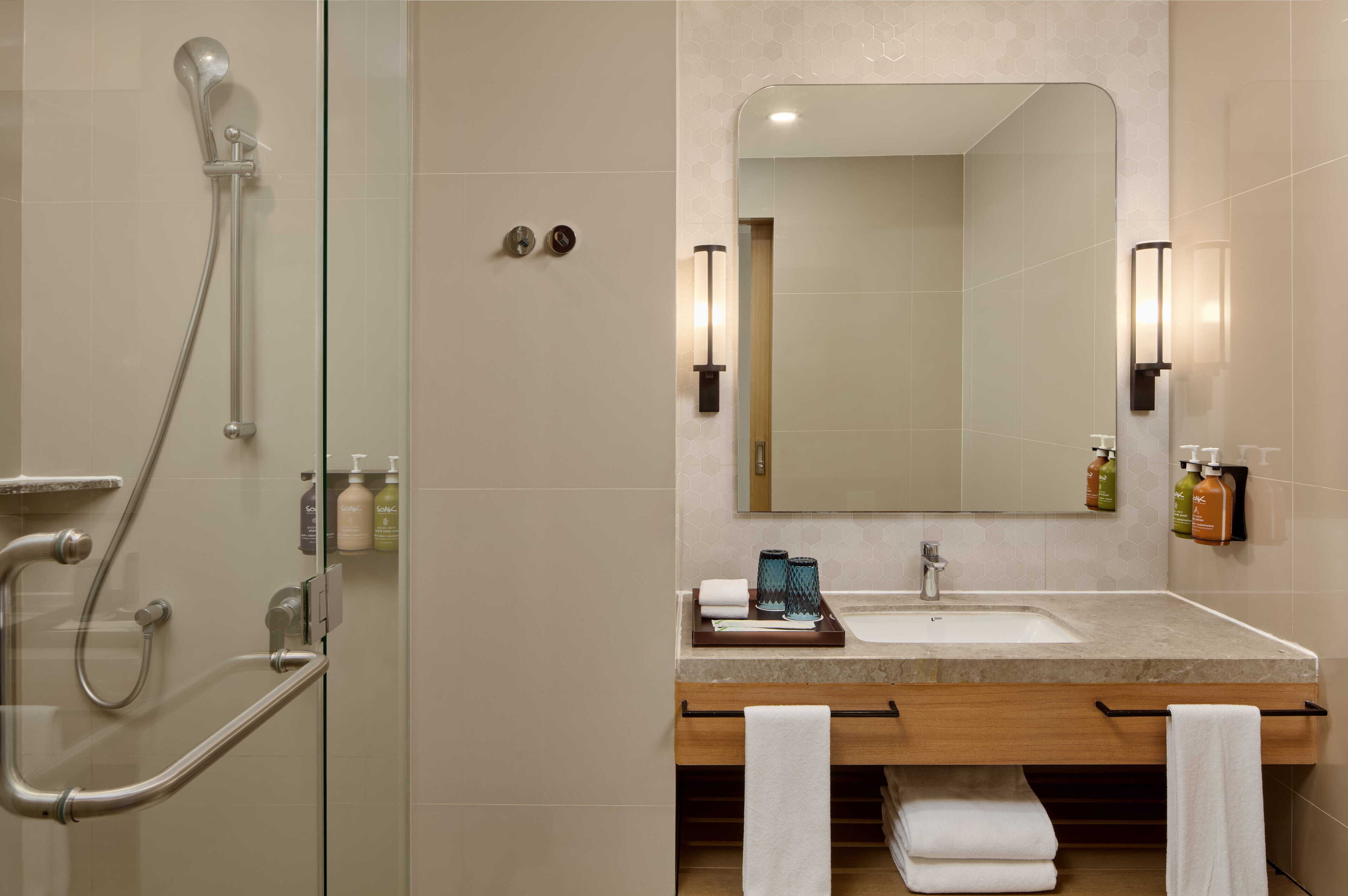 Une salle de bain moderne avec une douche à parois de verre, un grand miroir et un meuble-lavabo doté d’un évier et d’un porte-serviettes.