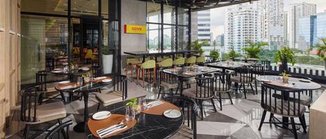 Un restaurant moderne avec des tables et des chaises rondes, une vue sur la ville et une enseigne indiquant « COVII ».