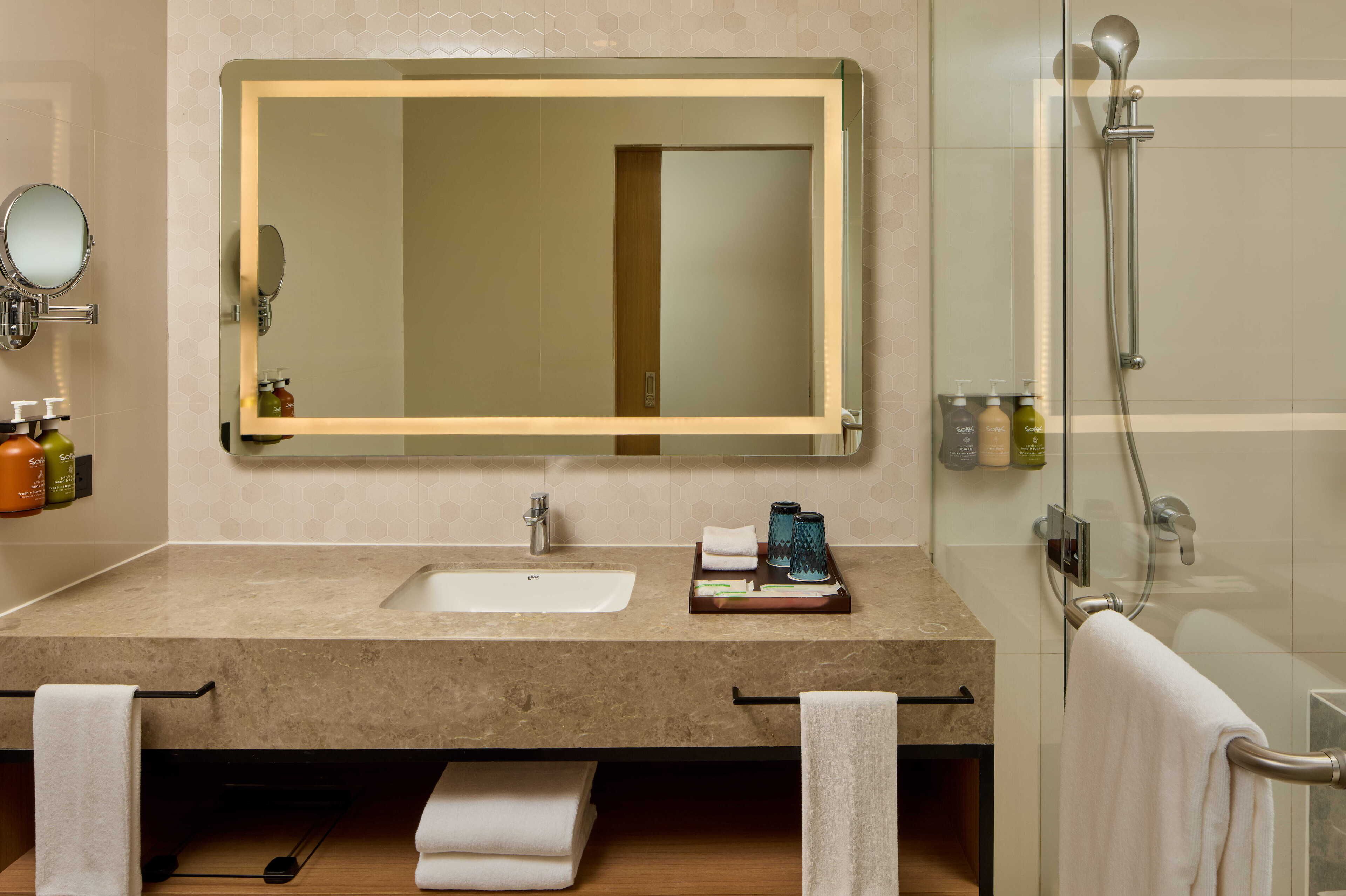 A bathroom with a large mirror, a sink, a shower, and a towel rack.