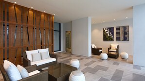 A modern lounge area with a brown wicker sofa, a glass coffee table, and white round ottomans. - Holiday Inn Cebu City by IHG (Cebu City)
