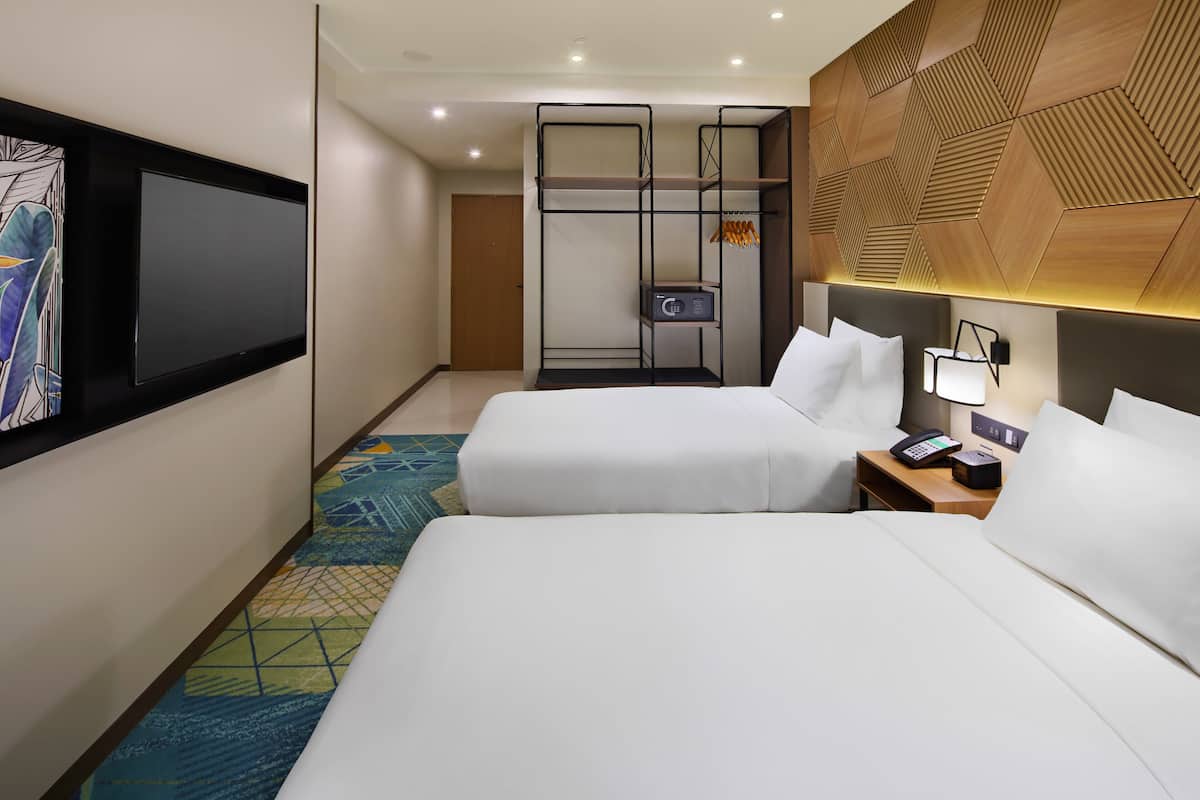 Une chambre d’hôtel avec deux lits, une télévision, un bureau avec une lampe et une armoire intégrée.