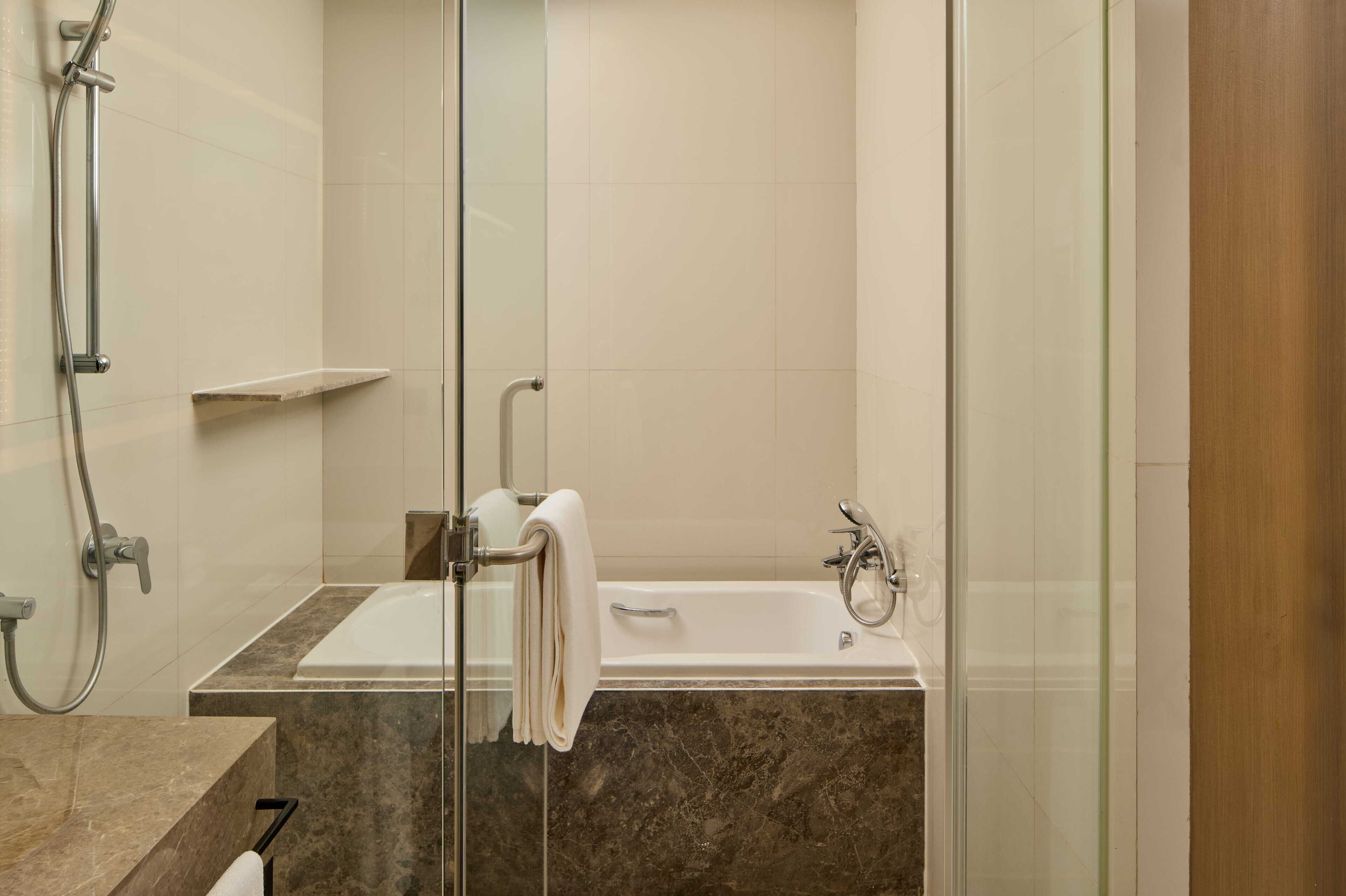 A modern bathroom with a glass-enclosed shower, a marble sink, and a white bathtub.