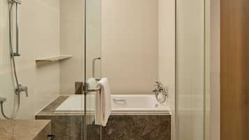 A modern bathroom with a glass-enclosed shower, a marble sink, and a white bathtub.