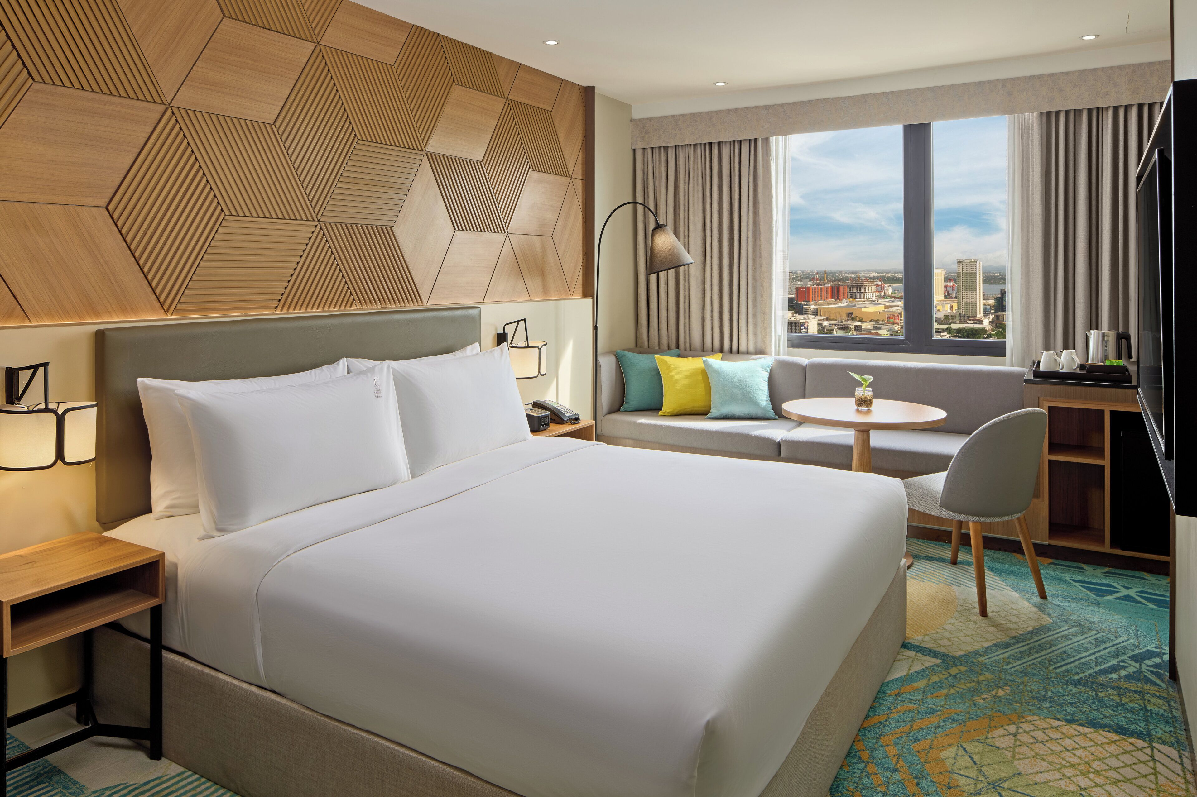 A hotel room with a bed, a sofa, a desk, and a view of the city.