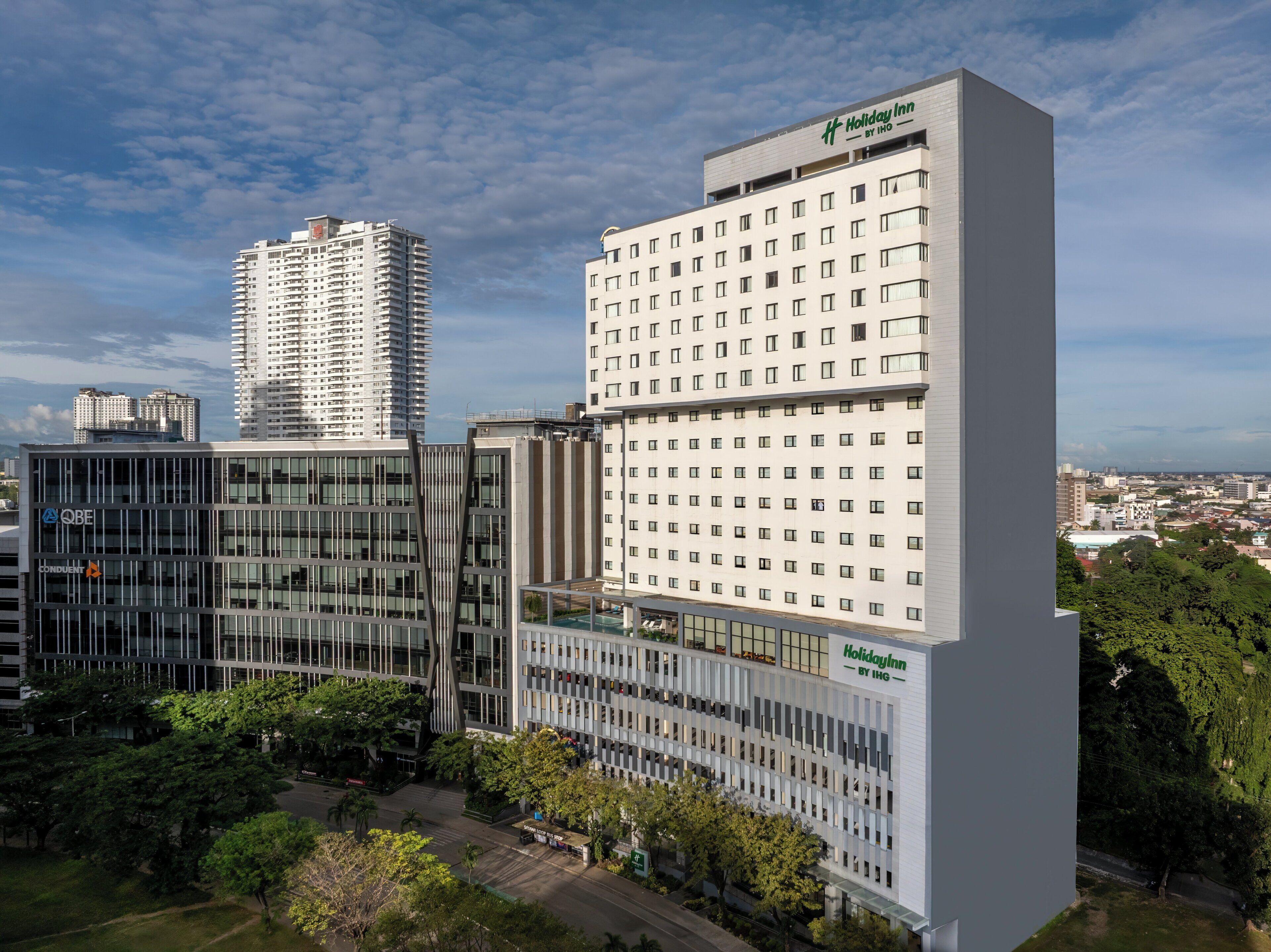 A Holiday Inn by IHG building with a modern glass facade, surrounded by other high-rise buildings and greenery.