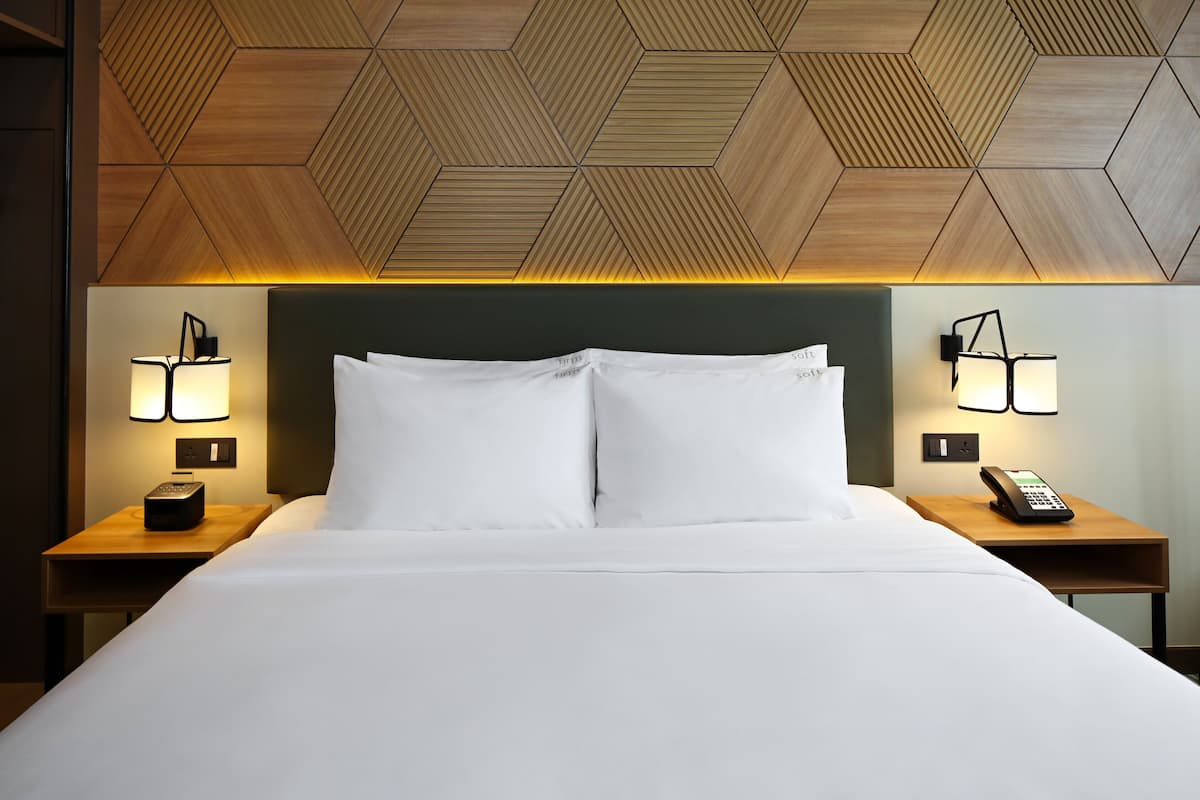 Une chambre d’hôtel avec un grand lit, deux tables de chevet avec des lampes, un plafond en bois orné de motifs géométriques et une tête de lit verte.