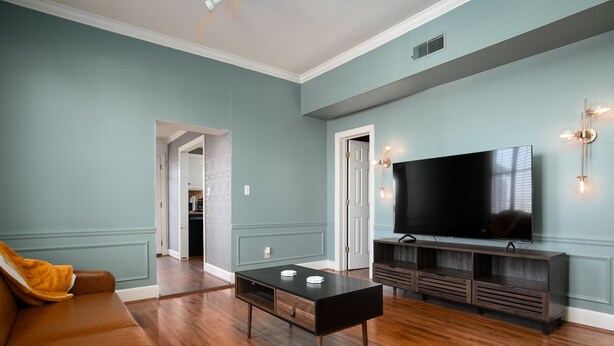 A living room with a brown leather sofa, a black coffee table, and a TV on a wooden stand. - Mid-Century Modern Townhouse with High Views (Birmingham)