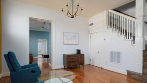 Un salon avec une table basse en verre, des fauteuils turquoise, un meuble en bois et un escalier avec des rampes blanches.