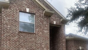 A two-story brick house with a garage door, a small window, and a visible chimney.