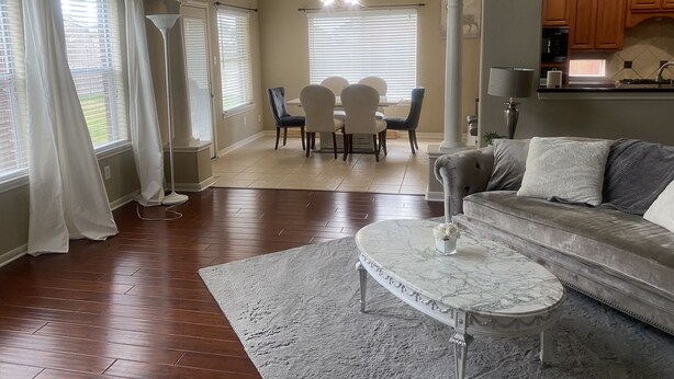 A spacious living room with a grey sofa, a marble coffee table, and a dining area with a white table and chairs.
