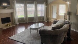 A living room with a fireplace, a sofa, a coffee table, and large windows with curtains.