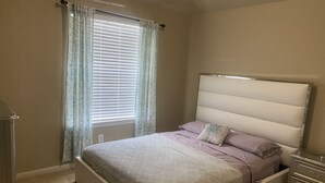 A bedroom with a bed, curtains, a nightstand, and a dresser.