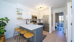 Una cocina moderna con armarios blancos, electrodomésticos de acero inoxidable y una isla central con taburetes.