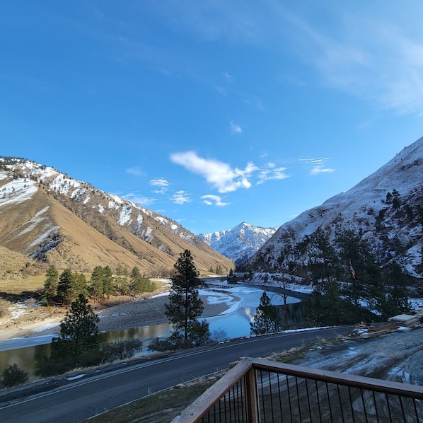 A mountainous landscape with a river, snow-covered peaks, and a clear sky.