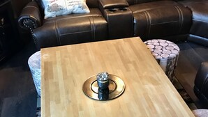 A wooden coffee table with a decorative centerpiece, surrounded by patterned ottomans and a leather sofa in a living room.