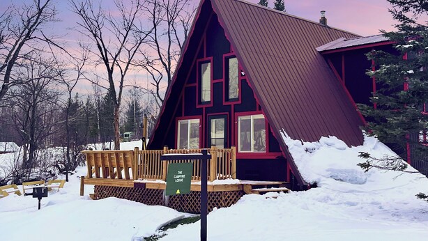 A cabin with a steeply pitched roof, a wooden deck, and a sign indicating it is a campfire lodge.
