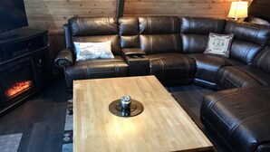 A cozy living room with a leather sectional sofa, a wooden coffee table, and a wood-burning stove.