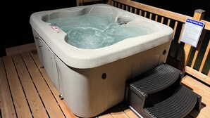 A hot tub with steps for access, a wooden deck, and a safety sign.