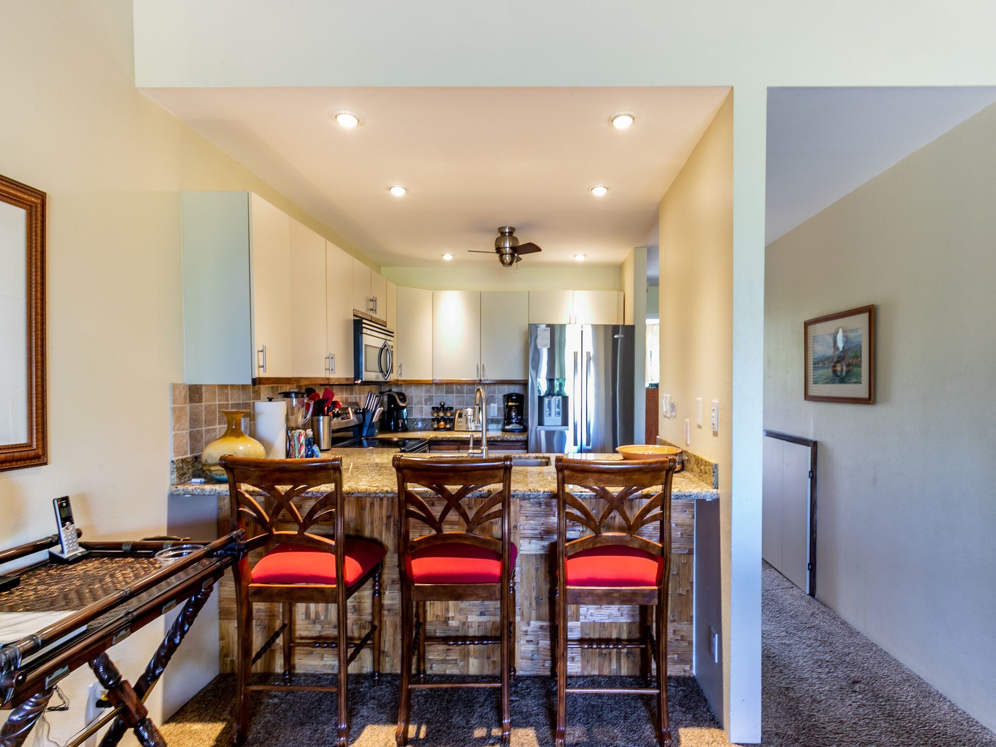 A kitchen with a central island, wooden chairs with red cushions, and a ceiling fan.