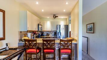 A kitchen with a central island, wooden chairs with red cushions, and a ceiling fan.