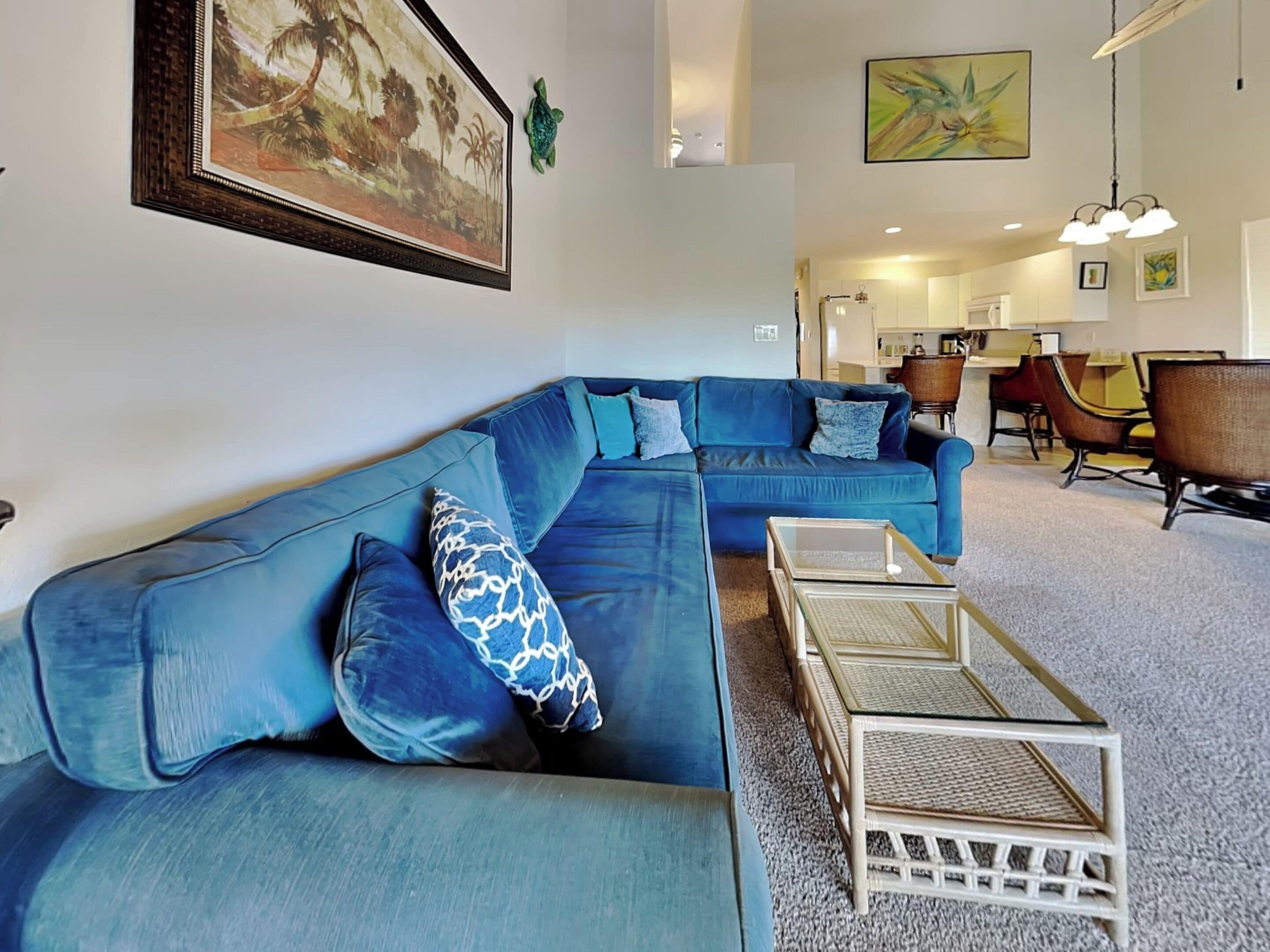 Ein Wohnzimmer mit einem blauen Ecksofa, einem Glastisch und einem Essbereich mit Stühlen und einem Tisch.