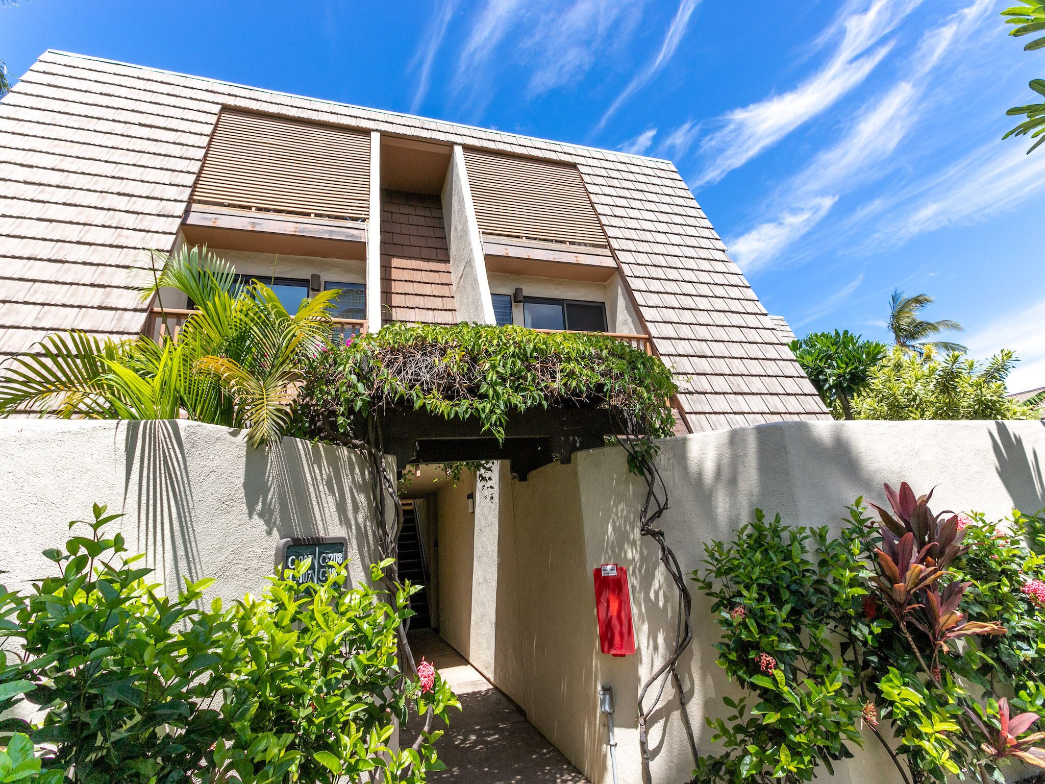 A building with a sloped roof, a covered entrance, and lush greenery around it.