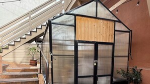 Una estructura pequeña y cerrada con fachada de madera y una puerta de metal negro, ubicada junto a una escalera que lleva a un balcón.